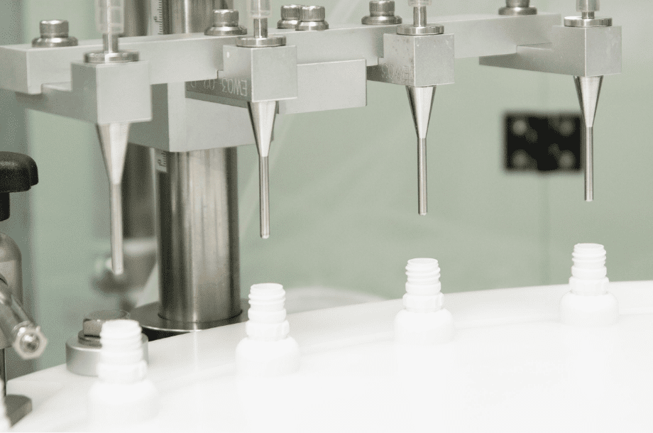 Filling nozzles dosing product into white bottles in D Block