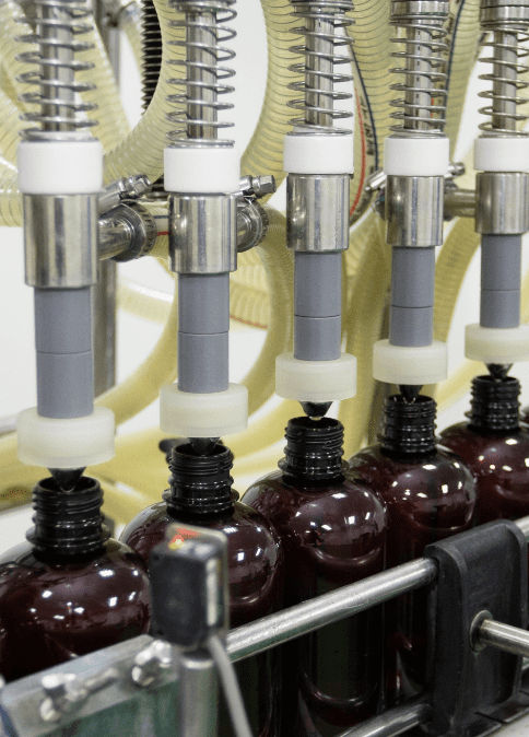 Filling nozzles dosing traditional herbal liquid into amber bottles