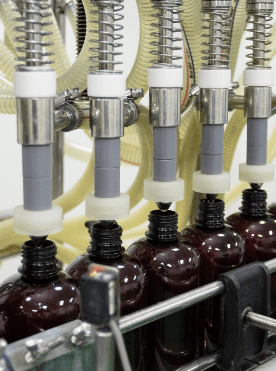 Filling nozzles dosing traditional herbal liquid into amber bottles